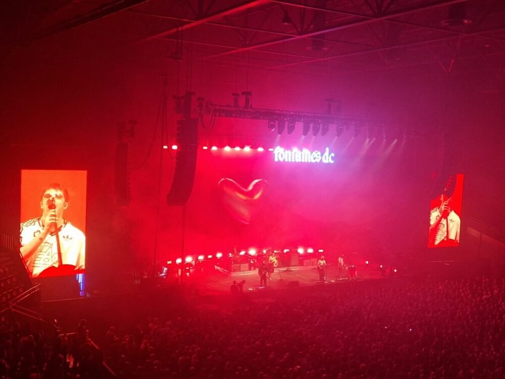 Fontaines D.C. debut "Demolition" live in Belgrade days after Serbia's student-led election win 2 Fontaines D.C. on a red-lit arena stage under a glowing "fontaines dc" sign, with Grian Chatten shown on a side video screen